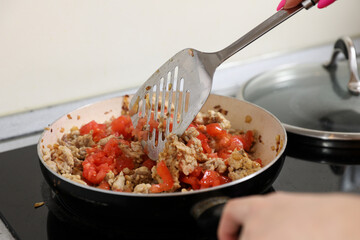 young housewife fry meat in a pan and electric stove. Cooking dinner at home.