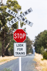 Red stop sign at a railway crossing on a country road running to the horizon. Outback Australia.
