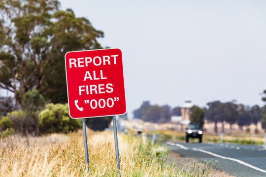 Red warning sign asking drivers on a lonely rural outback road to report all fires and dial triple 0 (000). Rural country road, Australia.