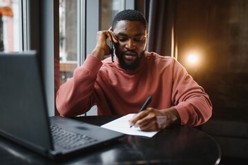 Businessman Using Phone Working On Laptop In Coffee Shop