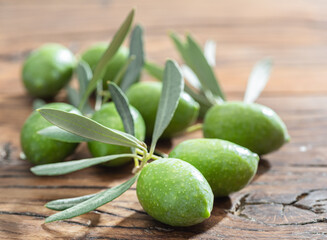 Green natural olives with olive leaves on a vintage old wooden table.