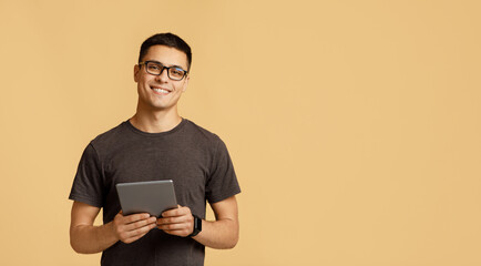 Cheerful young attractive man in glasses looks at camera, holds digital tablet on online lesson - obrazy, fototapety, plakaty