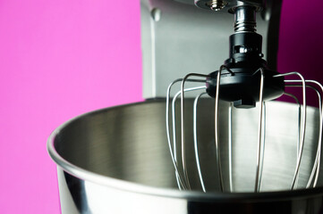 Chrome plated planetary mixer, whisk and bowl close up on pink background, kitchen helper