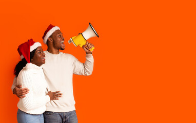Christmas Announcement. Happy Black Couple In Santa Hats Shouting With Loudspeaker