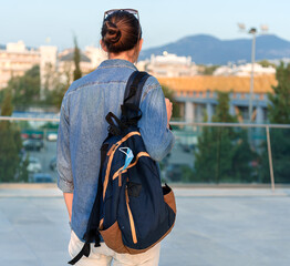 Fototapeta premium Young man with backpack and protective face mask inside standing outdoor with city at background