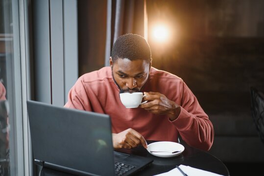 Portrait of happy african businessman sitting in a cafe and working on laptop