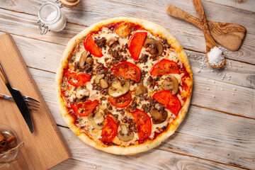 Top view on minced meat pizza with mushrooms and tomatoes on the wooden table