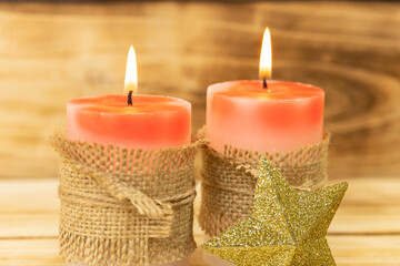 Christmas candles on wooden background, shallow depth of field. Two red candles are wrapped in a sack rope, next to a shining Christmas star.