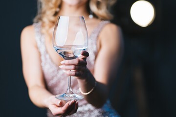 Portrait of funny lady in sequined evening dress holding glass of water in winter evening. with vintage cinematic light on dark background.