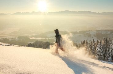 Happy Man with hood running in deep powder snow with snowshoes at sunrise. Snow is spraying and splashing. Allgau Alps, Bavaria, Germany.
