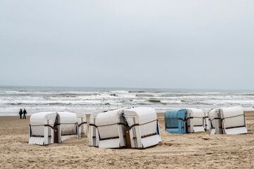 Fototapeta na wymiar Lonely winter cold seashore with empty beach cabins and walking people. Seascape in cold season.