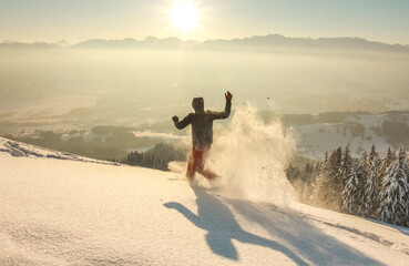 Happy Man with hood running in deep powder snow with snowshoes at sunrise. Snow is spraying and splashing. Allgau Alps, Bavaria, Germany.