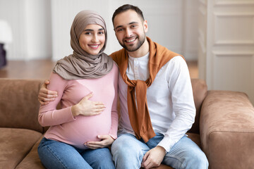 Happy Muslim Husband Hugging Pregnant Wife Sitting At Home