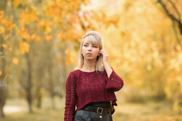 Blonde girl in a maroon sweater in the Park in autumn among the yellow leaves