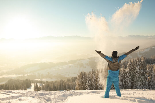 Happy Man standing in deep snow throwing snow into sunrise sunlight. Beautiful Winter Mountain Landscape. Allgau, Bavaria, Alps, Germany.