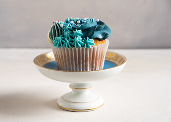 One pretty cup cake on a decorative china bowl. Decorated with blue butter icing
