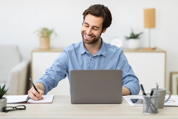 Cheerful Businessman Working At Laptop Taking Notes Sitting At Workplace