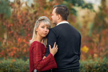 Fototapeta premium blonde girl in maroon sweater, brown-haired young man in blue sweater hug in the Park