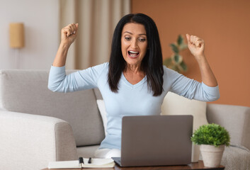 Excited mature woman screaming yes using laptop computer