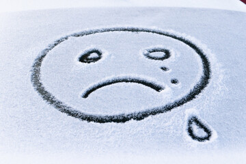 Fototapeta na wymiar image of a crying face emoji on the snow on the back window of a car on a bright frosty winter day