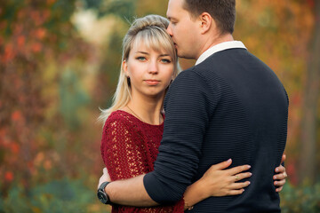 blonde girl in maroon sweater, brown-haired young man in blue sweater hug in the Park