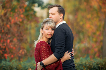 Fototapeta premium blonde girl in maroon sweater, brown-haired young man in blue sweater hug in the Park