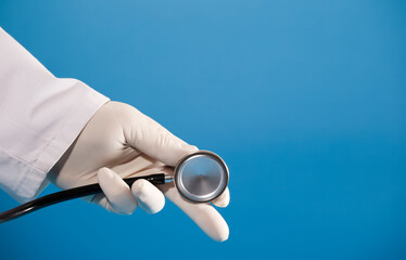 Stethoscope in doctor's hand with surgical glove and blue background.