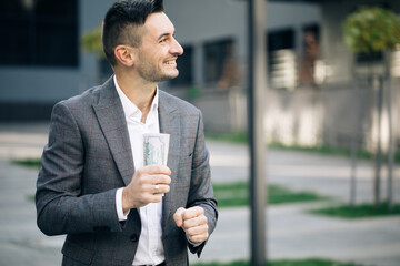 Happy rich successful man holds dollars outdoors. Portrait of satisfied businessman holds money....