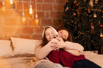 Happy mother playing with her 8 years daughter in the bedroom near the decorated Christmas tree