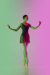 Light. Young and graceful ballet dancer isolated on gradient pink-green studio background in neon. Art, motion, action, flexibility, inspiration concept. Flexible ballerina, weightless jumps.