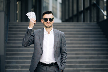 Lifestyle, richness, joy, success. Happy rich successful man holds dollars outdoors. Portrait of...