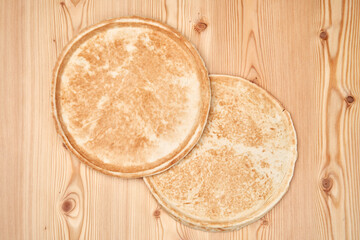 Two flat pizza dough on a wooden table, top view.
