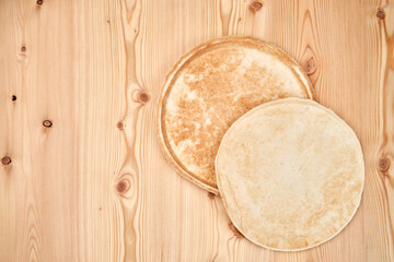 Two flat pizza dough cakes on a wooden table. One lies on the other. Top view with copy space.