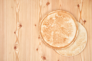 Two flat pizza dough cakes on a wooden table. One lies on the other. Top view with copy space.