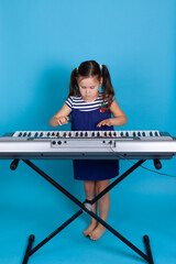 a full-length girl stands near the synthesizer and plays enthusiastically on it, isolated on a blue...