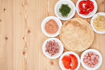 Slicing fresh food for pizza, with dough on a wooden background. Delicious homemade food. View from above.