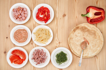 Fresh dough prepared for pizza with tomatoes and sliced pepper on a wooden board, close up