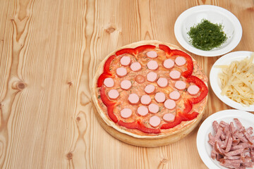 Making pizza surrounded by ingredients on a light wooden background. Close-up with copy space.