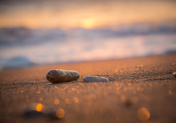 Two lonely stones are lying on the evening sandy beach. The sea is lapping in the distance. The...