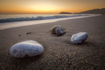 Fototapeta na wymiar Pebbles washed by the sea on a quiet sandy beach set you up for relaxation and meditation. In the background you can see the waves and the silhouette of the mountain with the ancient castle of Alanya