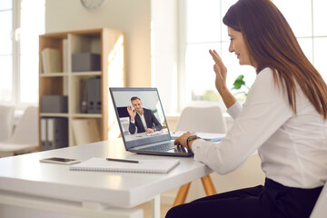 Smiling young business woman office worker in shirt sitting and greeting her director or partner online