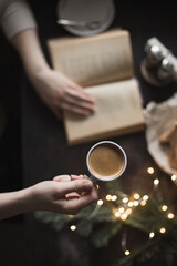 Fototapeta na wymiar Cup of espresso in girl's hand and book, dark photo, selective focus, cozy christmas winter photo, top view