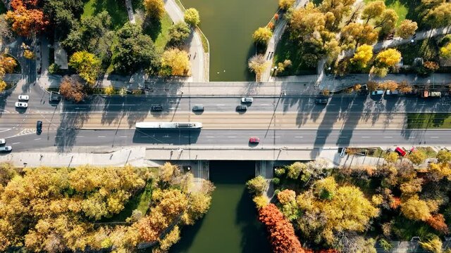 A road over the the lake with moving cars in the Titan park, multiple greenery. View from the drone, Bucharest, Romania