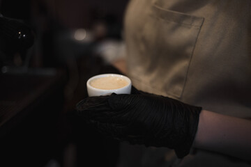 Fototapeta na wymiar Soft focus dark photo of barista wearing black medical gloves presses coffee to espresso. Coffee shop health protection