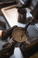 Soft focus barista in black medical gloves whips milk in coffee machine. Coffee shop pandemic, health protection