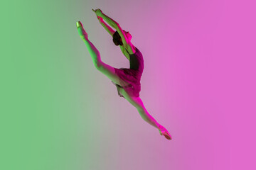 Flying. Young and graceful ballet dancer isolated on gradient pink-green studio background in neon. Art, motion, action, flexibility, inspiration concept. Flexible ballerina, weightless jumps.