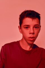 Close up portrait of teenaged disabled boy with cerebral palsy looking away, posing isolated over red light background