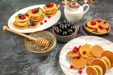 Side view of family breakfast with fruit pancakes honey in a bowl and black cherries on gray table