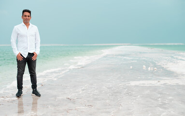Young businessman stand on the white beach of dead sea. Blue sea paradise for summer holidays. The...