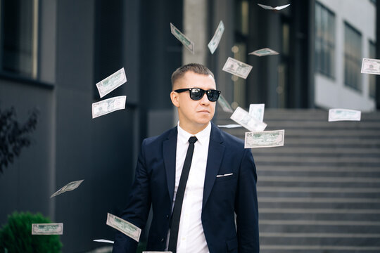 Money rain, falling dollars. Portrait shot of cheerful rich handsome businessman in glasses and suit throws money. Happy good looking man throwing dollars